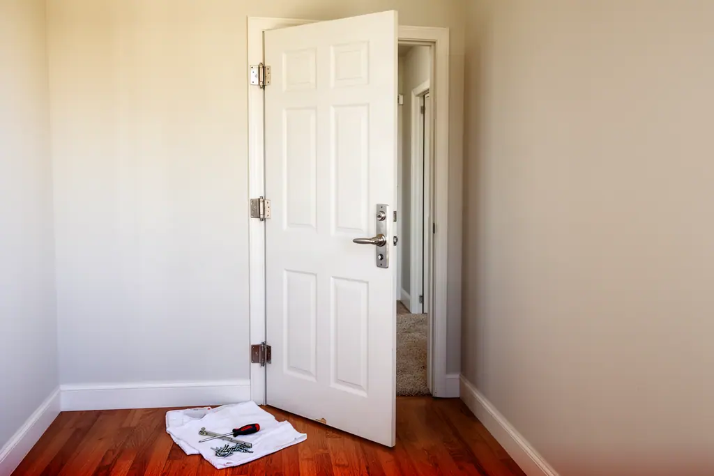 White six-panel interior door with a new brushed-nickel lever handle, with a screwdriver and screws on a cloth on the floor.